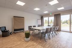 Hotelcamp Reinsehlen | Schneverdingen | Tagungsraum mit Tisch und acht Stühlen. Raumhohe Fenster, Pinwand und Moderatorenkoffer